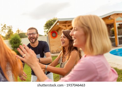 Group of cheerful young friends having fun at poolside summertime outdoor party, playing blind man's buff, running and chasing each other on the backyard lawn