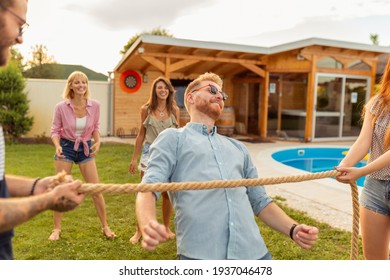 Group Of Cheerful Young Friends Having Fun At Summertime Outdoor Party By The Swimming Pool, Participating In Limbo Dance Contest, Passing Below The Rope While Dancing