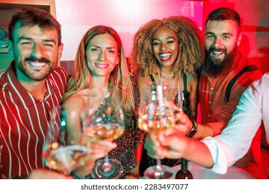 Group of cheerful young friends having fun at house party, making a toast raising glasses of wine towards the camera, dancing and drinking - Shutterstock ID 2283497077