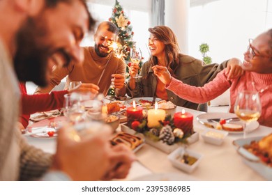 Group of cheerful young friends having Christmas dinner together at home, waving with sparklers and making a toast raising glasses of wine - Powered by Shutterstock