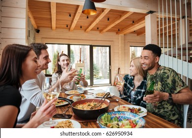 Group Of Cheerful Young Friends Having Dinner And Laughing At The Table At Home