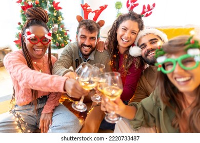 Group of cheerful young friends making a toast while drinking wine, having fun celebrating Christmas together at home - Shutterstock ID 2220733487