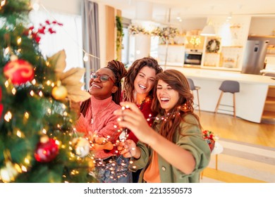 Group of cheerful young girl friends having fun spending winter holiday season together, decorating Christmas tree and home for Christmas and New Year - Powered by Shutterstock