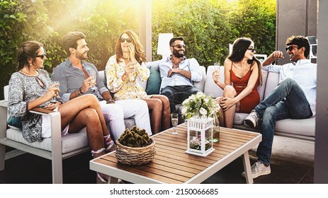 Group Of Cheerful Young People Carefree Sitting Together Drinking Wine At Luxury Garden - Friends Get Together Sitting On A Couch In The Terrace Backyard Having Fun Drinking Champagne