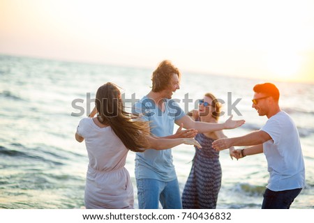 Group of cheerful young people dances having joined hands on the beach. Summer, waves, sea wind, sunset. Friends a lot of fun.