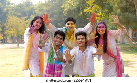 Group of cheerful young people happily wishing Happy Holi at a Holi party in a park. Happy Indian friends excitedly showing their palms covered in powder colors while celebrating Holi festival 