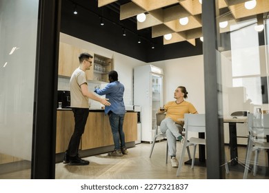 Group of cheerful young people talking and smiling during coffee break time in the office. Team of professional software developer relaxing in the canteen. - Powered by Shutterstock