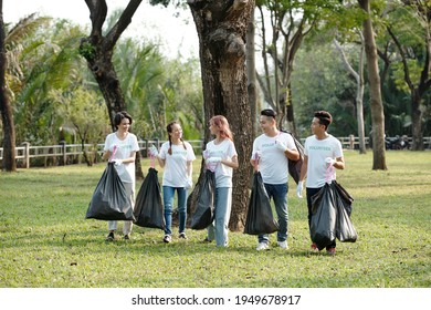 Group of cheerful young volunteers carrying bags of trash they picked on campus or in city park
