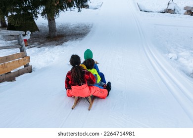 group of children in bright winter clothes riding one wooden sled going down snow slope - Shutterstock ID 2264714981