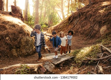 Group of children building camp in forest together. Boys and girls carrying sticks and walking