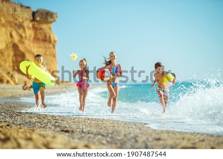 A group of children have fun playing at the sea. Children in bathing suits. Friends holding hands and running on the beach. High quality photo.