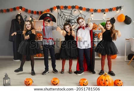 Group of children having fun and doing zombie dance at Halloween party at home. Bunch of happy kids dressed up in different spooky costumes walking and dancing like zombies in decorated living room