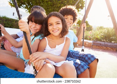 Group Of Children Having Fun On Swing In Playground