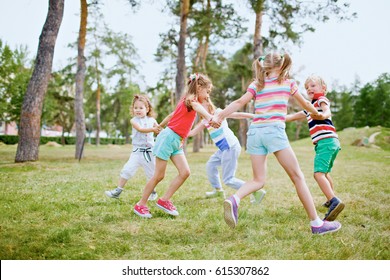 Group of children holding hands and dancing in circle on green lawn in park on beautiful summer day