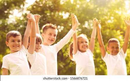 Group Of Children Holding Hands Up In Park On Sunny Day. Volunteering With Kids