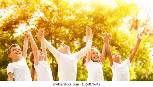 Group Of Children Holding Hands Up In Park On Sunny Day. Volunteering With Kids