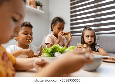 A group of children are joyfully eating sandwiches and salad at a dining table, highlighting the essence of a happy and healthy mealtime together. - Powered by Shutterstock