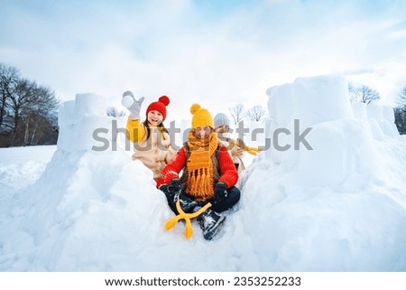 Group of children make snowballs for snowball fights. Children play in snow fort made of ice blocks. Active winter outdoor games.