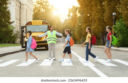 Group of children passing crosswalk on their way to school bus, diverse pupils cross the street with the crossing guard blocking traffic, boys and girls going home after classes, copy space - Powered by Shutterstock