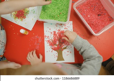 Group of children playing with colored rice from the sensory box. Painting exercise. Baby's sensory educational kit. Top view.