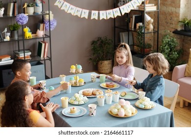 Group Of Children Playing Rock Paper Scissors Game While Sitting At Table With Sweet Food In Living Room At Birthday Party