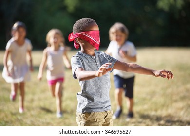 Group of children plays blind man's buff at the park in summer