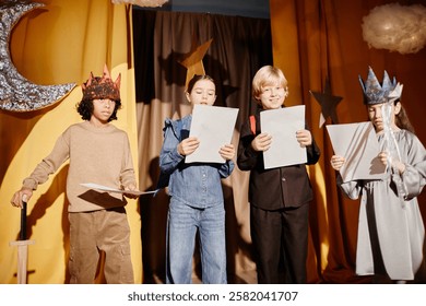 Group of children reading scripts during school play performance, holding papers, and wearing unique costumes with star and moon decorations positioned in background