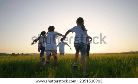 group of children run across the field on the grass. happy family kid lifestyle dream concept. children running in a field with tall grass on the sunset. girls holding hands in the foreground