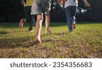 group of children run in the park on the grass. happy family kid dream concept. children with bare feet run on the grass in the park at sunset. bare feet group of kids run lifestyle in the park