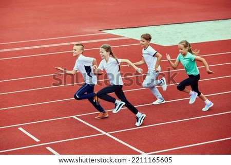 Group of children running on treadmill at the stadium or arena. Little fit boys and girls in sportswear training as athletes outdoor. Concept of sport, fitness, achievements, studying, goals, skills