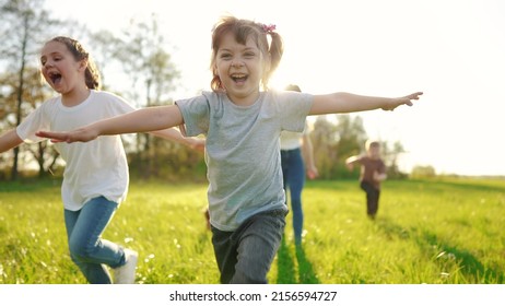 group of children running in the park. happy family baby kid dream concept. kindergarten. children hands to the sides play pilots plane run on the grass in sun the summer in the park