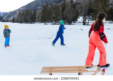 group of children children running in the snow valley against forest and mountain background with one wooden sled - Powered by Shutterstock