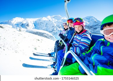 Group Of Children Ski Friends Sit On Chairlift Lifting On The Mountain Top Peak On Sunny Day