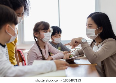 A Group Of Children Students Wearing Medical Masks In The Classroom. An Asian Woman Teacher And Students Were Discussing The Lesson. Concept Of Prevention Of The Coronavirus Outbreak And New Normal