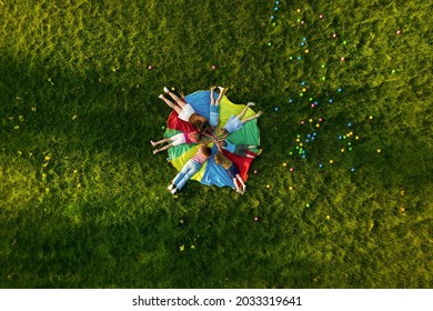 Group of children with teachers holding hands together on rainbow playground parachute in park, top view. Summer camp activity - Powered by Shutterstock