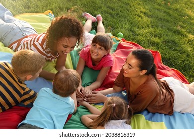 Group of children with teachers holding hands together on rainbow playground parachute outdoors. Summer camp activity - Powered by Shutterstock