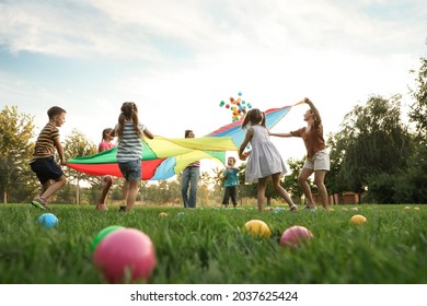 Group Of Children And Teachers Playing With Rainbow Playground Parachute On Green Grass, Low Angle View. Summer Camp Activity