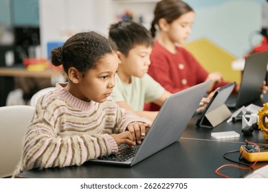 Group of children using laptops for educational activities in classroom equipped with modern technology while deeply focused on their tasks