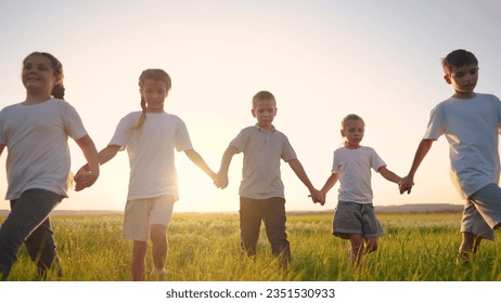 group of children walk across the field on the grass. lifestyle happy family childhood dream concept. kids walking in a field with tall grass on the sunset and holding their lifestyle hands - Powered by Shutterstock