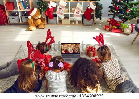 A group of children watching a video chat with Santa using a laptop in a decorated room during Christmas. Boys and girls 8-9 years talking with Santa Claus have a computer camera in a home.
