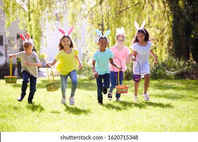 Group Of Children Wearing Bunny Ears Running To Pick Up Chocolate Egg On Easter Egg Hunt In Garden - Powered by Shutterstock