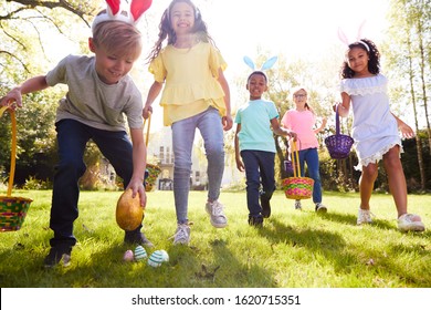 Group Of Children Wearing Bunny Ears Running To Pick Up Chocolate Egg On Easter Egg Hunt In Garden - Shutterstock ID 1620715351