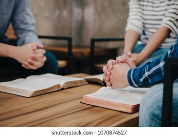 group of christian  sitting around wooden table with open blurred bible page and praying to God together