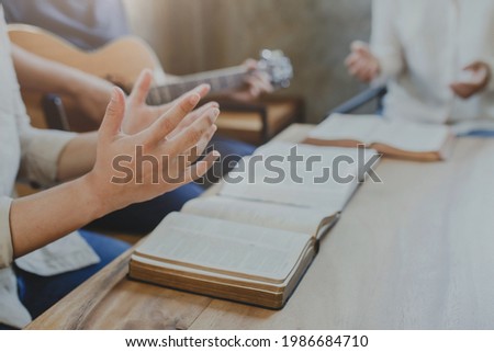 A group of Christian young man worship god while playing guitar and sings a song from a Christian hymn book with his friends at home, Christian family worship concept