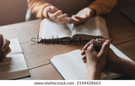 A group of Christians sit together and pray around a wooden table with blurred open Bible pages in their homeroom. Prayer for brothers, faith, hope, love, prayer meeting