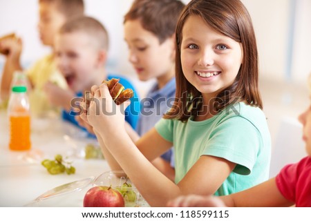 Group of classmates having lunch during break with focus on smiling girl with sandwich