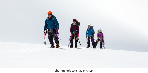 Group Of Climbers Approaching To Summit
Four People Staying On Mountain High Altitude Snowfield Sporty Clothing And Safety Climbing Gear Mature Male Guide And Young Female Athletes