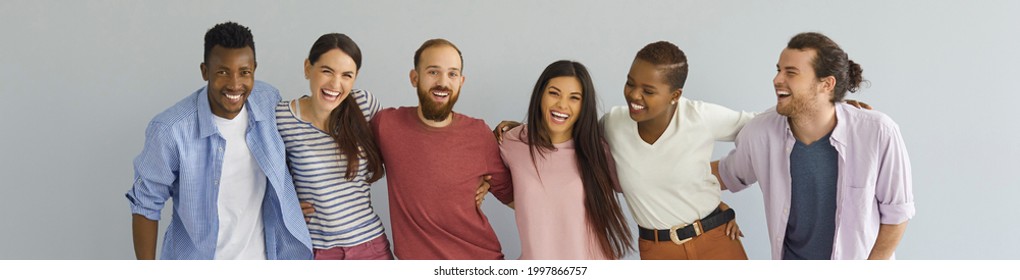 Group of close friends. Diverse team of happy cheerful sociable outgoing black and Caucasian young people in their 20s twenties in casual style clothes standing together against light grey background