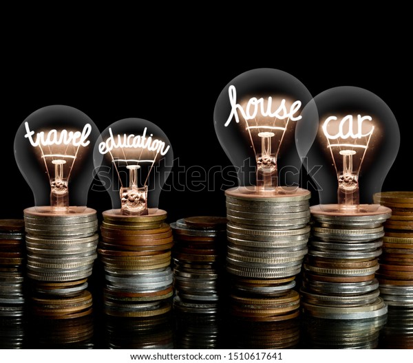 Group of coin rows and light bulbs with\
shining fibers in a shape of House, Car, Education and Travel words\
isolated on black background. Concept of Money Saving, Investment,\
Mortgage and Insurance.
