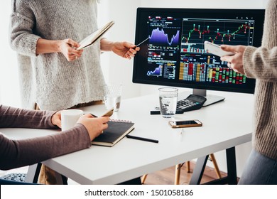 A group of colleagues discussing recent stock exchange trends pointing to the stock exchange screen showing trading graphics